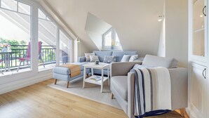 A modern loft bedroom with a sloped ceiling, large windows, a cozy seating area, and a built-in wardrobe. - Das Appartement Senskin für 2 Personen in Ruhiger Lage in Westerland (Sylt)