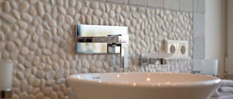 A bathroom with a pebble-textured wall, a white sink, and a modern faucet.