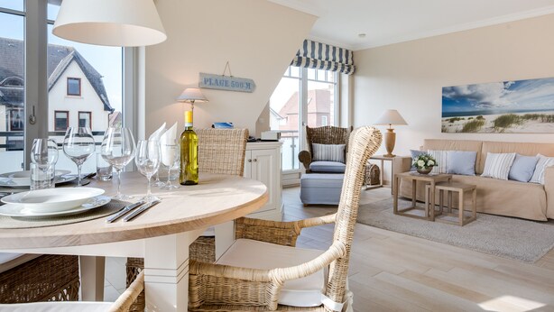 A dining area with a round table, wicker chairs, and a bottle of wine. There is a sign on the wall that reads "PLACE 500 M".
