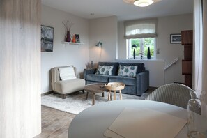 A living room with a sofa, armchair, coffee table, and a dining table.
