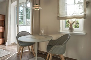 A room with a round table, two wicker chairs, a vase with flowers, and a window with a view of greenery.