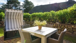 An outdoor patio with a table, chairs, a striped sofa, and a potted plant. - Top Lage. Luxuriöse Ausstattung. Wellness im Hause (Wenningstedt-Braderup (Sylt))
