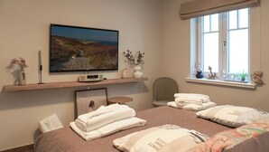 A bedroom with a bed, pillows, a TV, a window, and a shelf with decorative items. - Top Lage. Luxuriöse Ausstattung. Wellness im Hause (Wenningstedt-Braderup (Sylt))