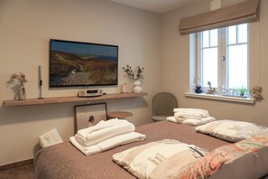Quarto com cama, almofadas, televisão, janela e prateleira com objetos decorativos.