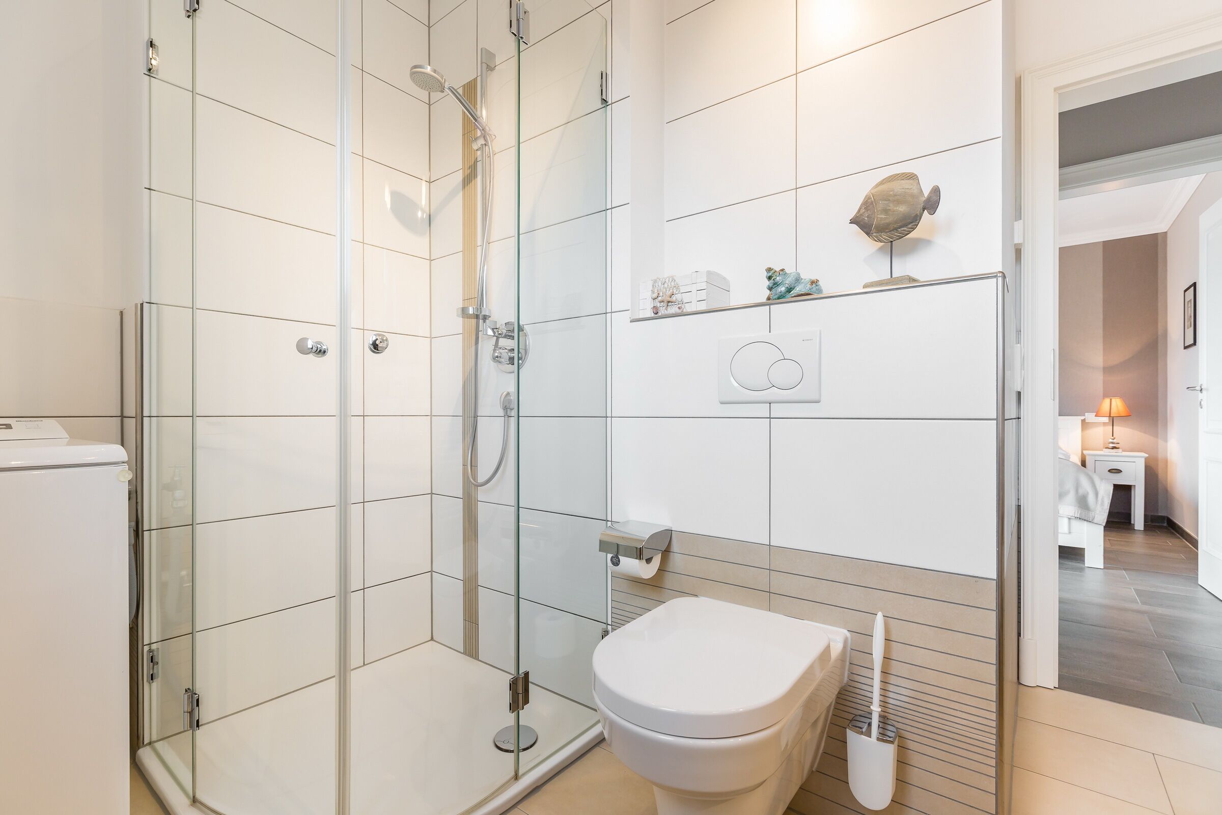 Ein modernes Badezimmer mit einer Duschkabine aus Glas, einer weißen Toilette und einem kleinen Regal mit Dekoration.