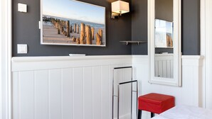 Ein Badezimmer mit einem großen gerahmten Bild von einem Strand, einem Spiegel, einem roten Hocker und einem Handtuchhalter.