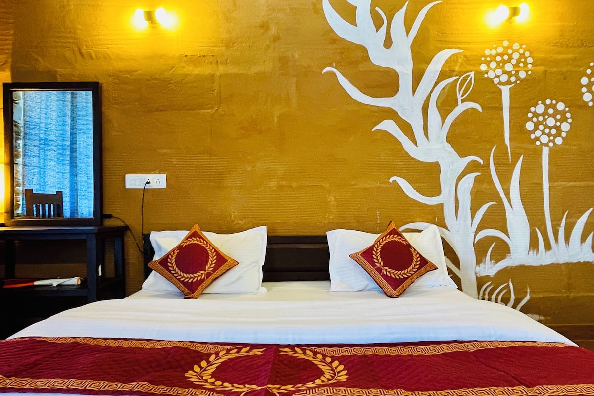 A hotel room with a large bed, two decorative pillows, a nightstand with a lamp, and a wall mural.