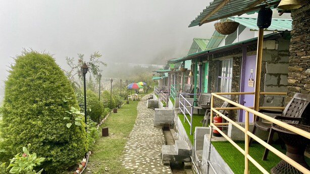 A pathway leading to a building with a stone facade, outdoor seating, and a view of the surrounding greenery. - Family in the Hills by Nature's Glamping (Kosiyakutoli)