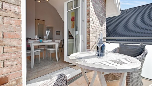 A patio area with a round table and wicker chairs, a dining table with chairs, and a brick wall.