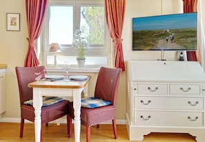 Un comedor con una mesa, sillas, un televisor y una ventana con cortinas.