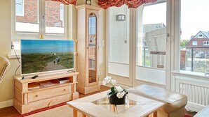 En stue med tv, møbler af træ, et glasbord og udsigt udad.
