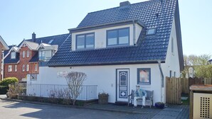 Et toetagers hus med mørkt tag af fliser, en lille veranda og en bænk udenfor.
