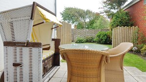 Un espace extérieur aménagé avec des meubles en osier, une table en verre et un auvent.