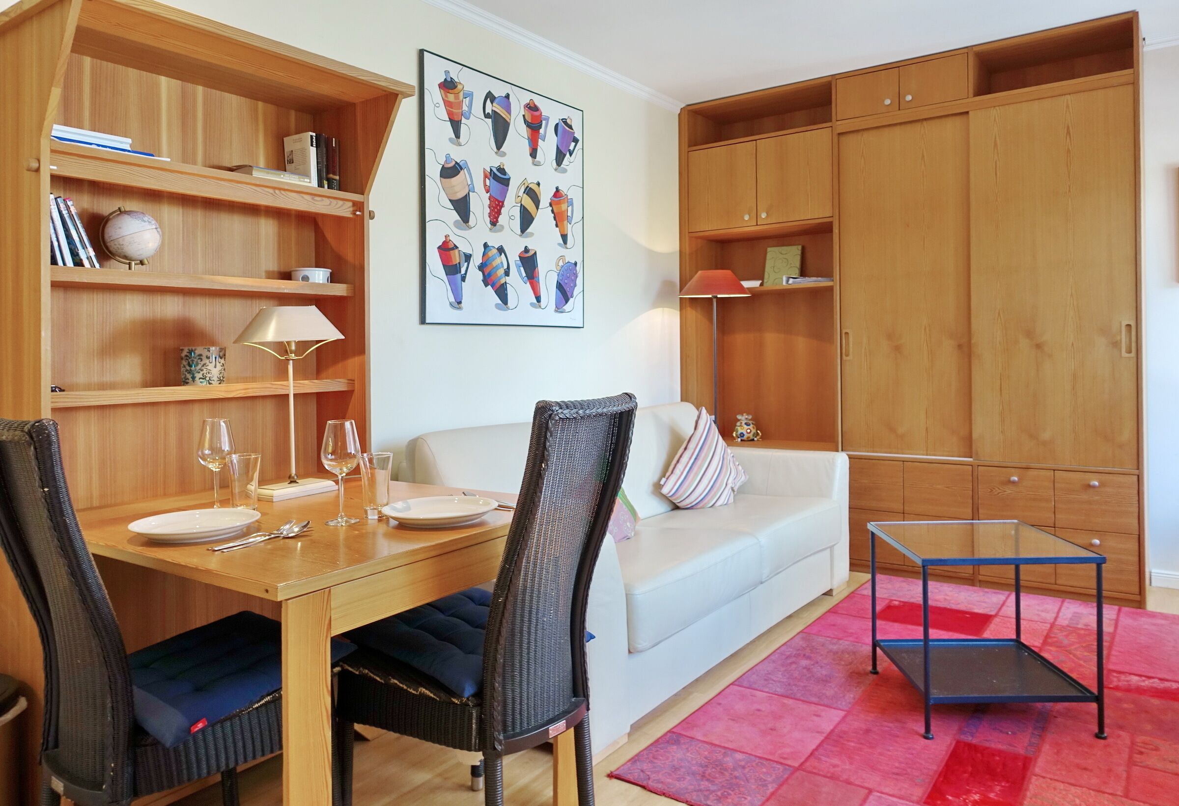 Uma sala de estar moderna com área de jantar, móveis de madeira, mesa de centro de vidro e tapete vermelho estampado.