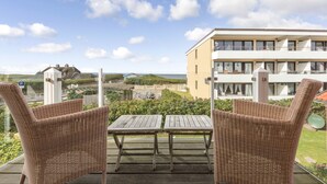 A balcony with wicker furniture and a view of a building with multiple balconies and a beach in the background. - Sunsets & a lot More (Wenningstedt-Braderup (Sylt))