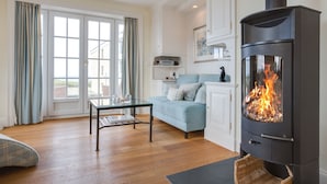 A living room with a sofa, a glass coffee table, a fireplace, and a view through large windows. - Sunsets & a lot More (Wenningstedt-Braderup (Sylt))