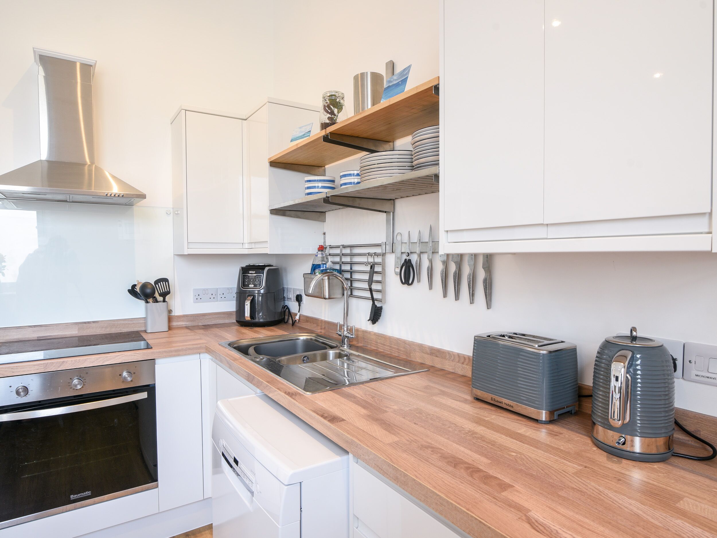 Cocina moderna con armarios blancos, electrodomésticos de acero inoxidable y encimeras de madera.