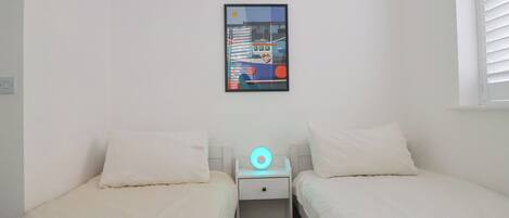 Un dormitorio con dos camas, una mesita de noche, un cuadro colgado en la pared y una decoración de guirnalda roja y azul.