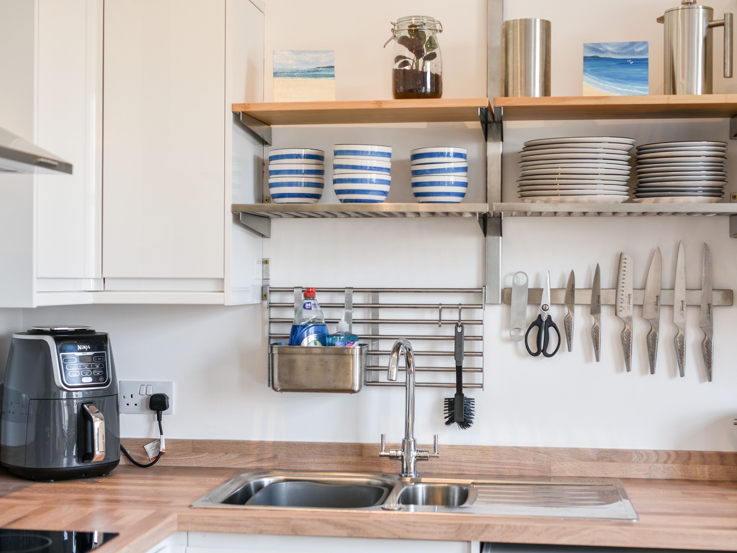 A kitchen with a stainless steel sink, a coffee maker, and utensils hanging on the wall.