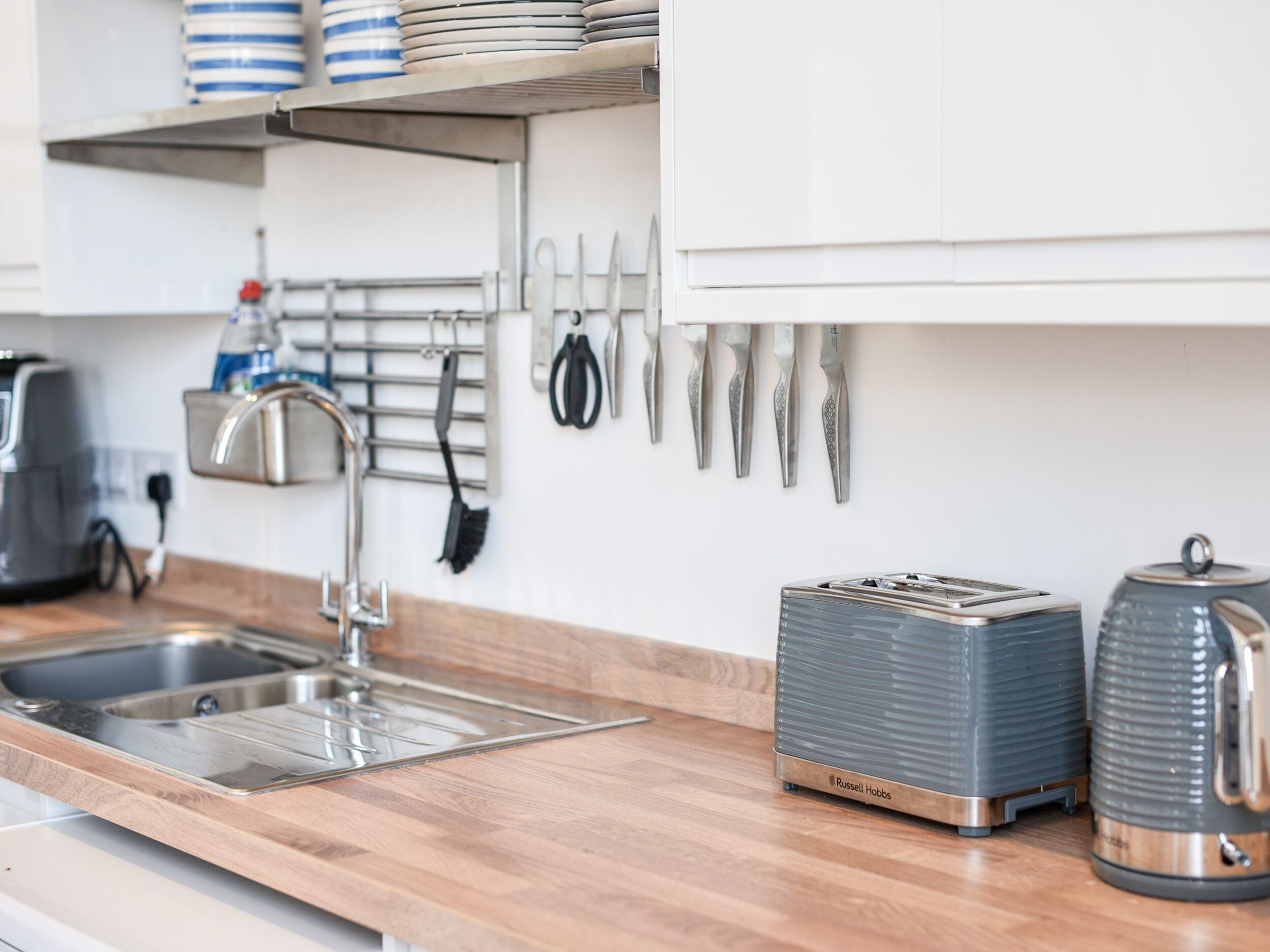 A kitchen with a wooden countertop, a sink, a toaster, and a kettle.