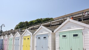 Una fila di casette da spiaggia colorate con porte numerate, una scala che conduce a un livello superiore e un cielo sereno.