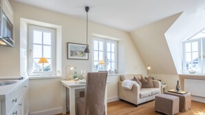 A modern loft apartment with a kitchen, dining area, and living space. It features large windows, a dining table, a sofa, and a small coffee table. - Sie Suchen Nach Einem Domizil, Dass Strandnah Gelegen Ist? (Wenningstedt-Braderup (Sylt))