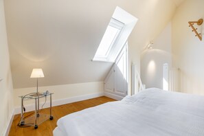 Un dormitorio con tragaluz, una mesita de noche con lámpara y una cama.