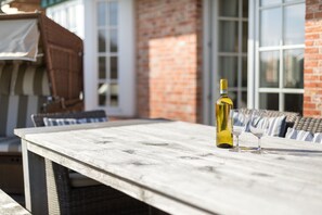 A wooden table with a bottle of wine and two glasses, set against a brick wall and large windows. - Strand, Meer & Luxus (Wenningstedt-Braderup (Sylt))