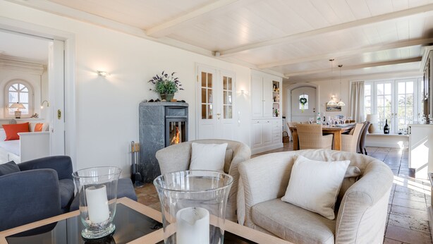 A spacious living room with a fireplace, a dining area, and a kitchen visible through an open door. - Strand, Meer & Luxus (Wenningstedt-Braderup (Sylt))
