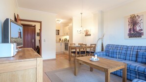 Ein Wohnzimmer mit Couchtisch aus Holz, einem blauen Sofa und einem Essbereich mit Holzsesseln.