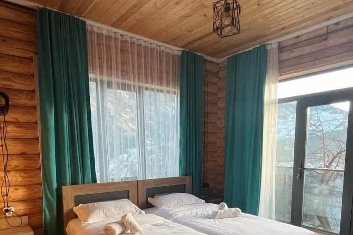 A wooden-paneled bedroom with a large bed, a nightstand, and a window with curtains.