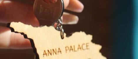A hand holding a keychain with a wooden piece shaped like a map and the text "ANNA PALACE".