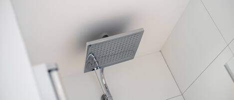 Una ducha moderna con cabezal cuadrado, grifería de cromo y una luz en el techo.