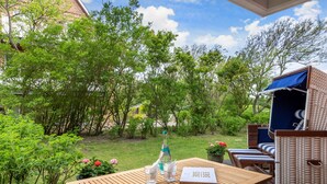A wooden table with a bottle and glasses, a sign with numbers, and wicker furniture in a garden setting. - Idyllische Lage, Ebenerdig im Erdgeschoss mit Terrasse und Garten (Wenningstedt-Braderup (Sylt))