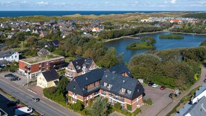 An aerial view of a residential area with houses, a road, and a lake. - Idyllische Lage, Ebenerdig im Erdgeschoss mit Terrasse und Garten (Wenningstedt-Braderup (Sylt))