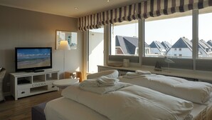 Quarto de hotel com televisão, aparador com tema de cinema, duas camas com lençóis brancos, janela com vista para casas e uma cobertura de cama listrada.