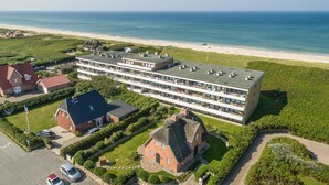 Um hotel moderno com vários andares, terraço no telhado e vista para a praia e oceano.