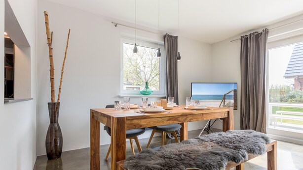Ein Essbereich mit Holztisch, Stühlen, einer Bank, einer Vase und einem Fernseher.