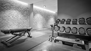 Ein Fitnessraum mit einer Bank, Hanteln und einem an der Wand befestigten Rack.