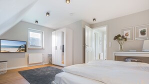 Ein Schlafzimmer mit einem großen Bett, einem Fenster mit Blick auf den Strand, einer weißen Kommode und einem kleinen Tisch mit einer Vase.