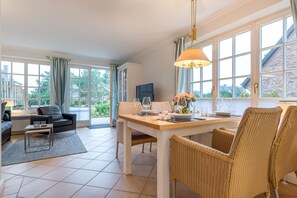 Un coin repas avec une table dressée pour quatre personnes, entourée de chaises en osier, et un téléviseur en arrière-plan.