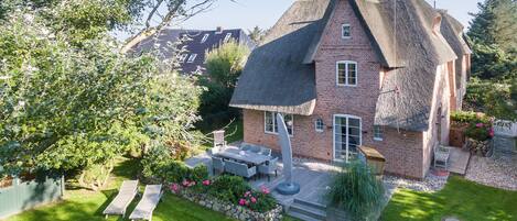 A house with a thatched roof, a patio with outdoor furniture, and a well-maintained garden.