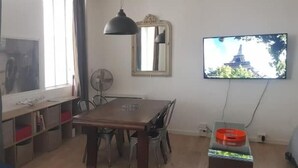 Ein Essbereich mit Holztisch, Stühlen, Deckenventilator, Wand-Fernseher und einem Vorhangfenster.