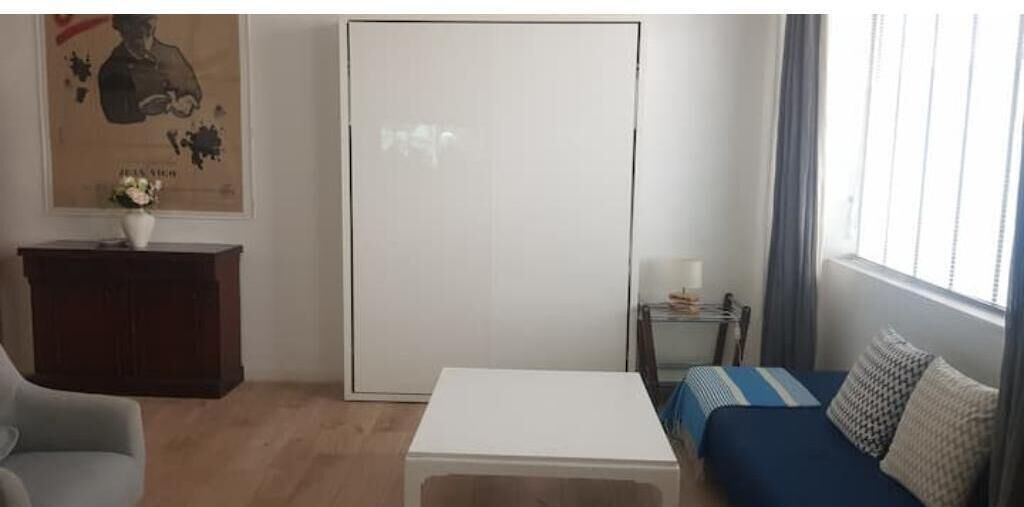 A room with a white sofa, a small table, a white cabinet, and a large window with curtains.
