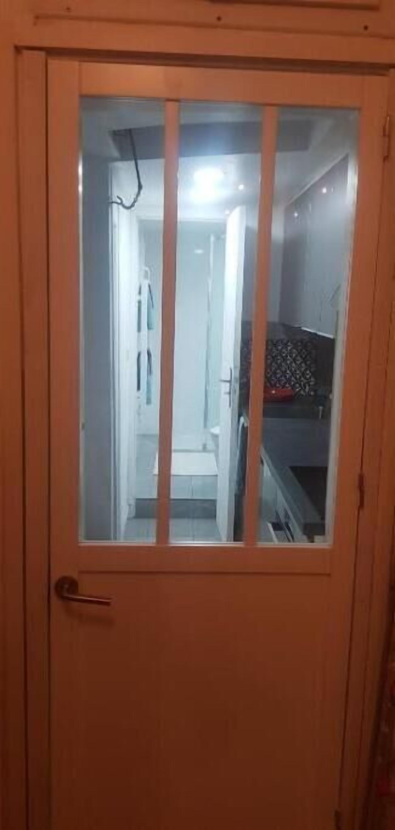 A door with a frosted glass panel, leading to a narrow hallway with a staircase and a patterned wall.