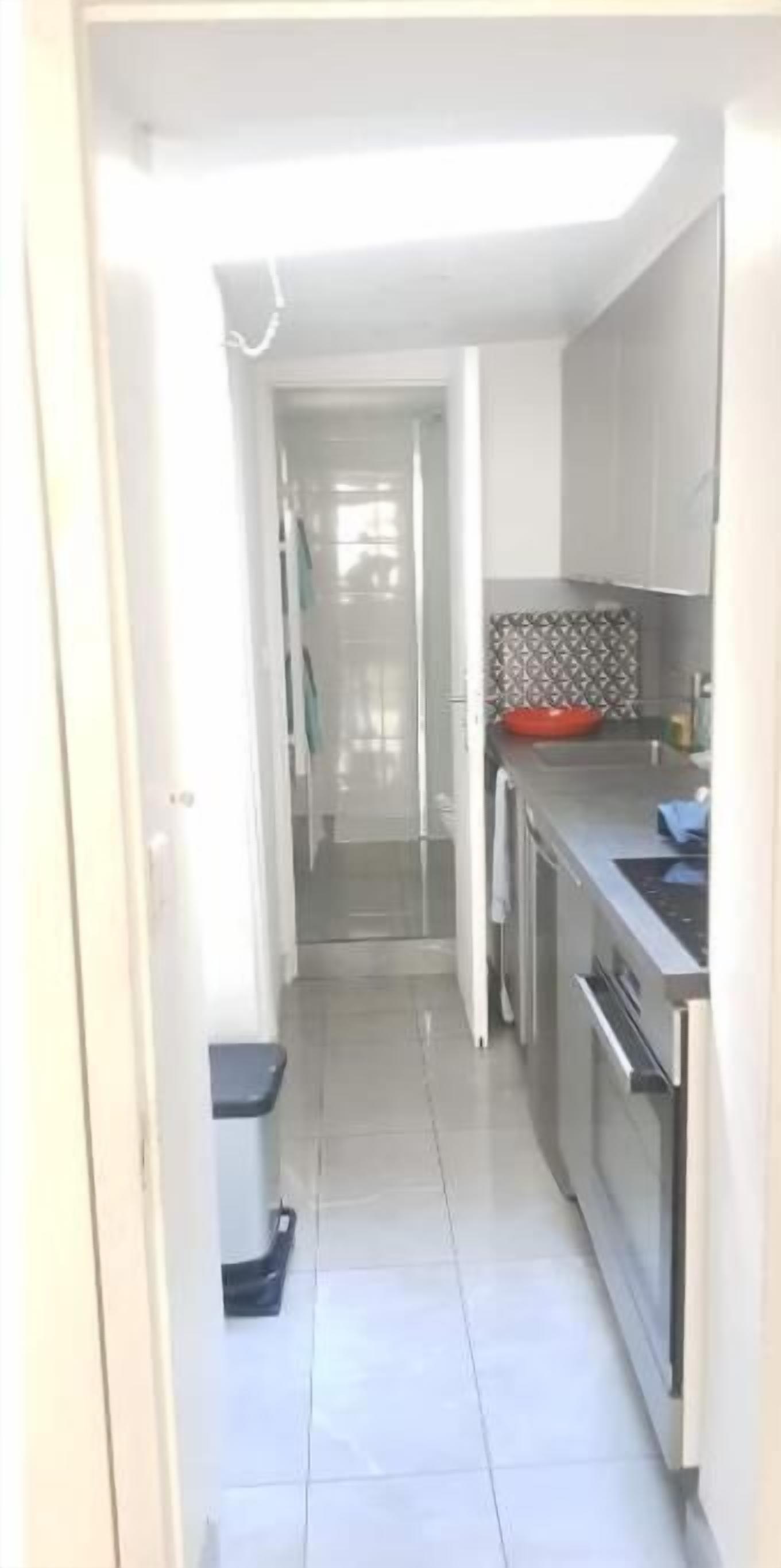 Una cocina estrecha y bien iluminada con electrodomésticos modernos, un salpicadero de azulejos y una puerta visible que conduce a otra habitación.