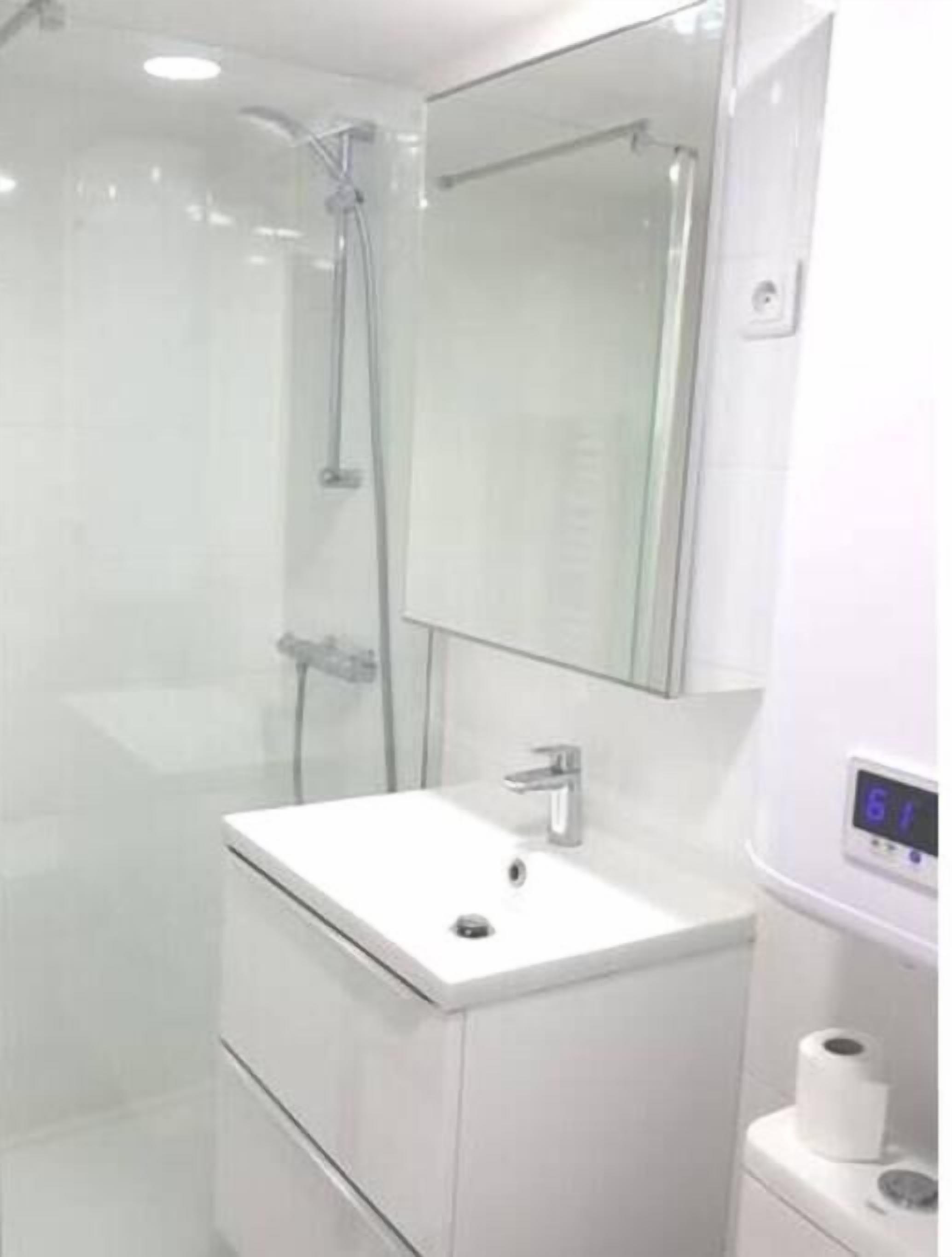 A modern bathroom with a glass-enclosed shower, a white sink, and a digital thermostat.