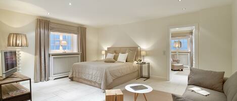 A modern bedroom with a large bed, bedside tables, a TV, and a sofa.