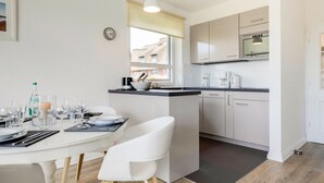 Une cuisine moderne avec des armoires blanches, un four encastré et un coin repas comprenant une table et des chaises blanches.