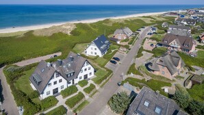 Vue aérienne d’une zone résidentielle côtière, avec des maisons, une plage et un ciel dégagé.